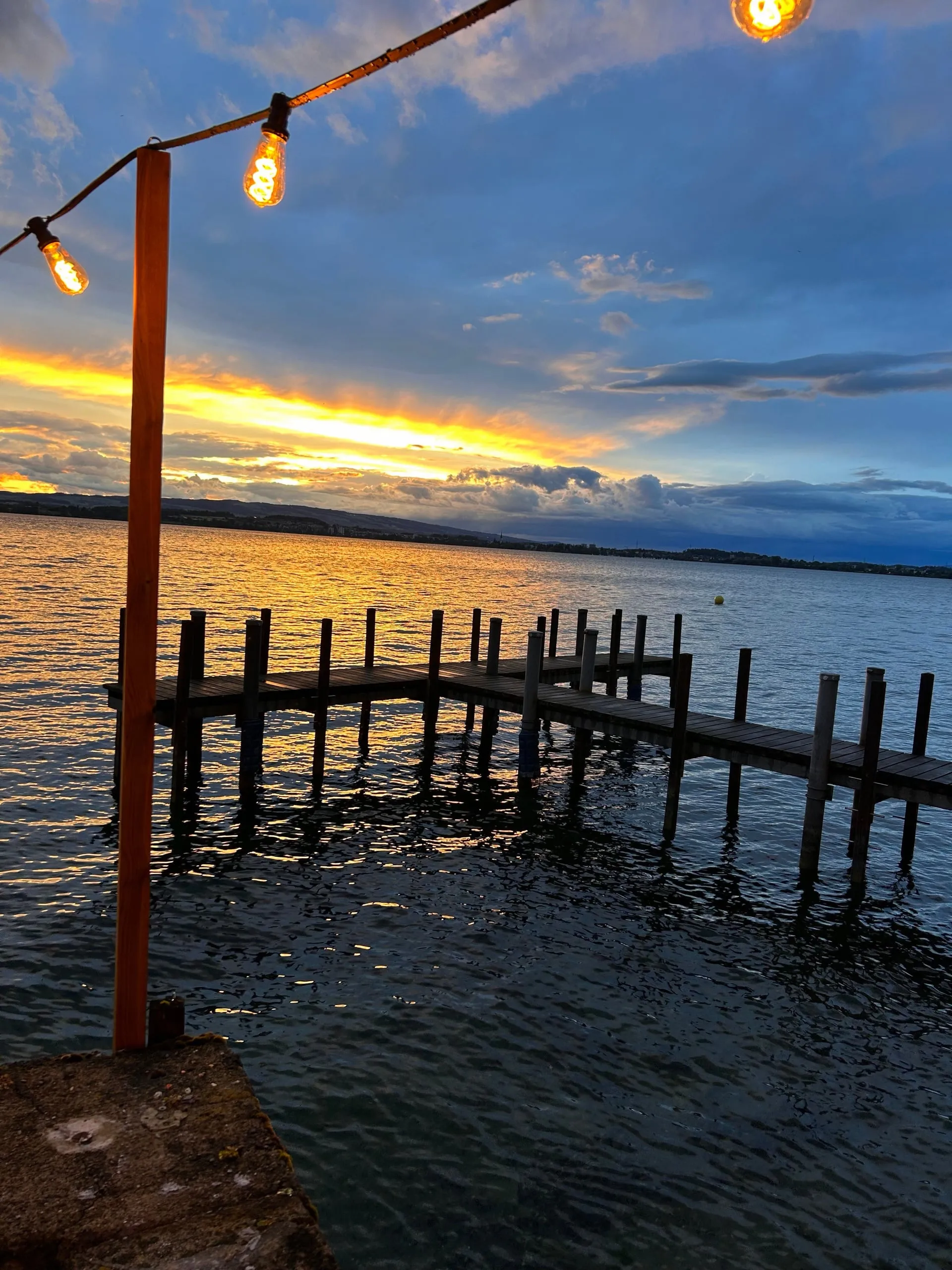 Sonnenuntergang über dem Zugersee mit Steg und Lichterkette